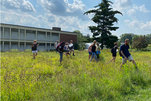 Students walk through tall prairie plants outside a campus building.