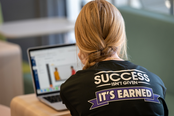 student facing laptop with shirt that says success isn't given it's earned width=