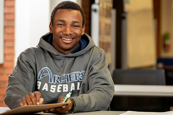 A smiling STLCC student seated in a classroom holds a clipboard and marker. width=