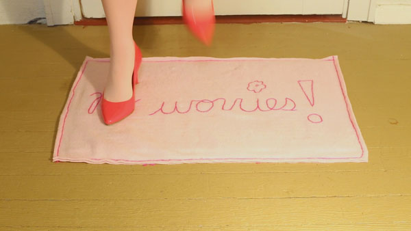 A lower leg of a woman in high heals stepping on a mat the says "no worries"