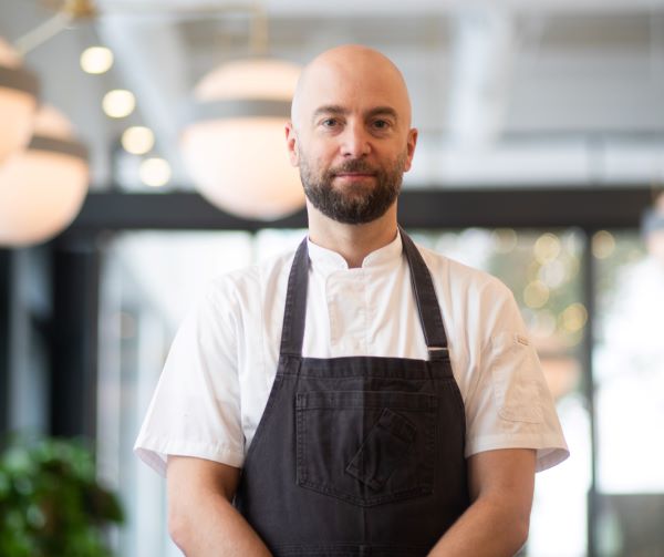 Chef Greg Vernick in white chef coat and black apron, standing in restaurant
