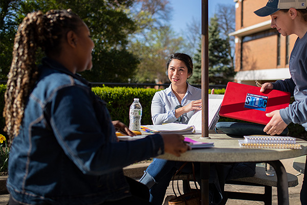 Florissant Valley students sit at an outdoor picnic table with a tutor