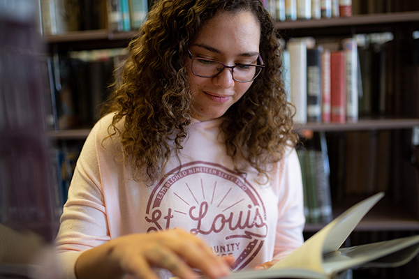 Student in the Florissant Valley library browses through a book 