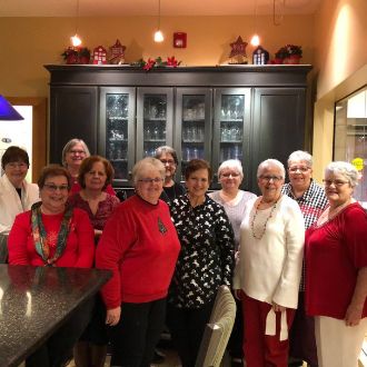 The Lunch Bunch is a group of retired, longtime employees of St. Louis Community College at Florissant Valley. Pictured here, the ladies are standing together in a kitchen, dressed in holiday colors of red, white and green. Photo courtesy of The Lunch Bunch.