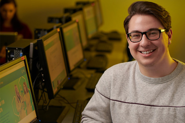 Student smiling while sitting at a computer in a computer lab 