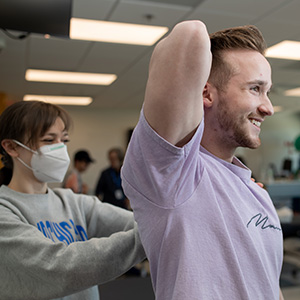 Patient stretches arms with help of physical therapy student
