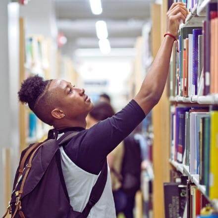 black student looking through books at the library to study for his program