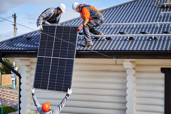 Three people installing solar panels on a residential building